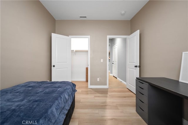 bedroom with a walk in closet, light wood-style flooring, baseboards, and visible vents