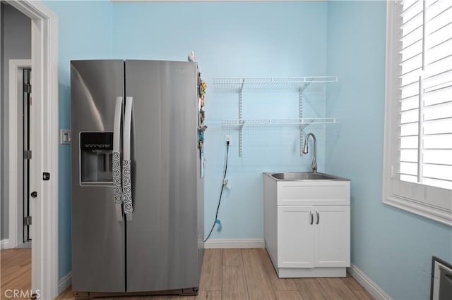 kitchen with baseboards, stainless steel fridge with ice dispenser, light wood-style floors, white cabinetry, and a sink