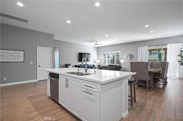 kitchen featuring a kitchen island with sink, a sink, stainless steel dishwasher, open floor plan, and white cabinetry