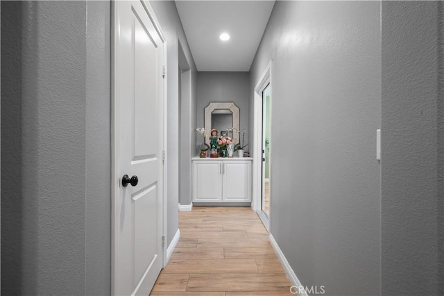 hallway with baseboards, light wood-style flooring, and a textured wall