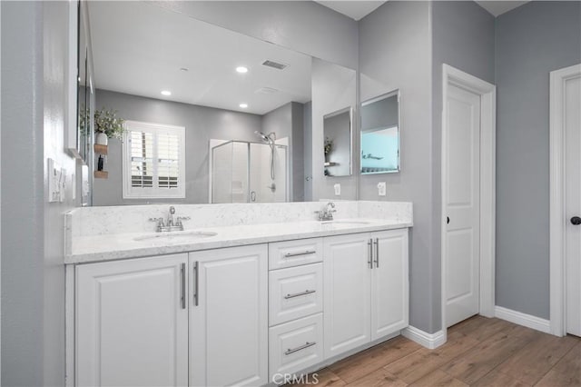 full bath with double vanity, a stall shower, wood finished floors, and a sink