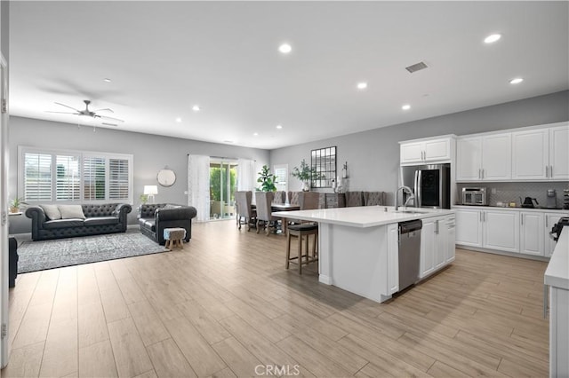 kitchen featuring open floor plan, appliances with stainless steel finishes, an island with sink, and light wood-style floors