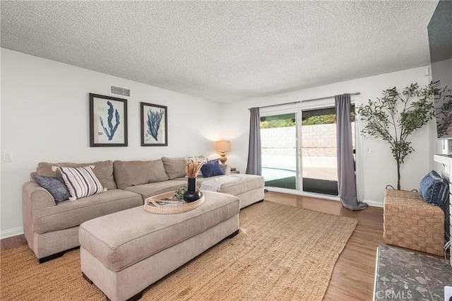 living room with visible vents, light wood-style flooring, a textured ceiling, and baseboards