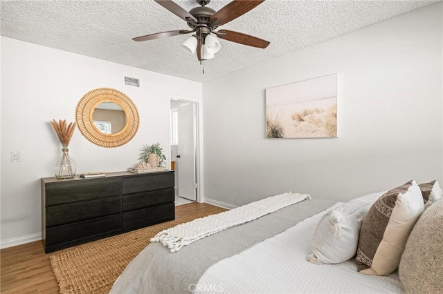 bedroom featuring a ceiling fan, baseboards, wood finished floors, visible vents, and a textured ceiling