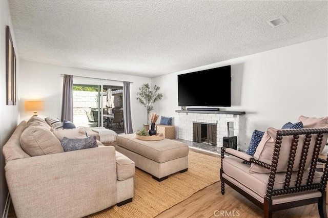 living area with visible vents, a brick fireplace, a textured ceiling, and wood finished floors