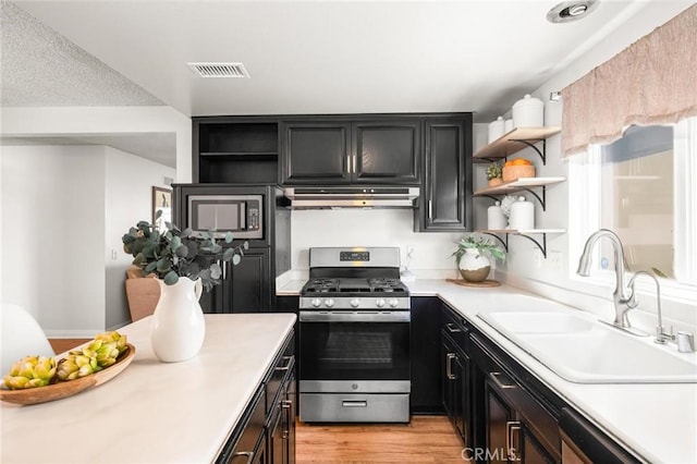 kitchen featuring open shelves, under cabinet range hood, a sink, dishwashing machine, and stainless steel range with gas stovetop