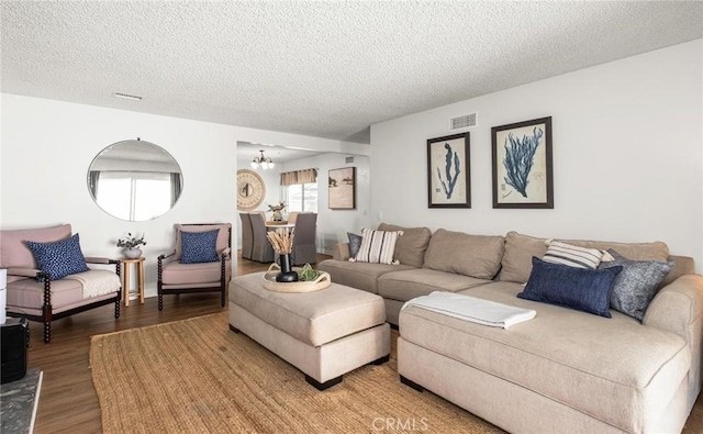 living room with wood finished floors, visible vents, a chandelier, and a textured ceiling