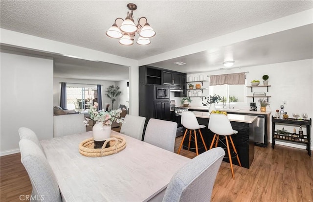 dining room with an inviting chandelier, baseboards, light wood finished floors, and a textured ceiling