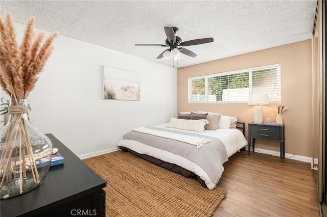 bedroom featuring ceiling fan, a textured ceiling, baseboards, and wood finished floors