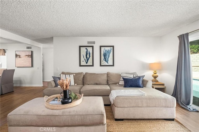 living room featuring visible vents, a textured ceiling, baseboards, and wood finished floors