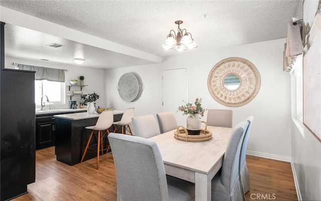 dining room with an inviting chandelier, visible vents, light wood-type flooring, and baseboards