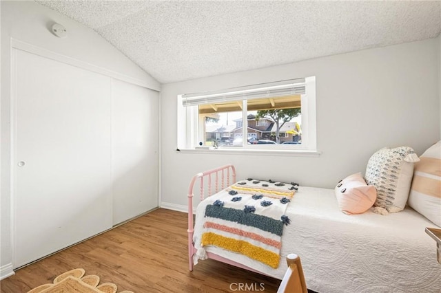 bedroom featuring a closet, a textured ceiling, wood finished floors, and vaulted ceiling