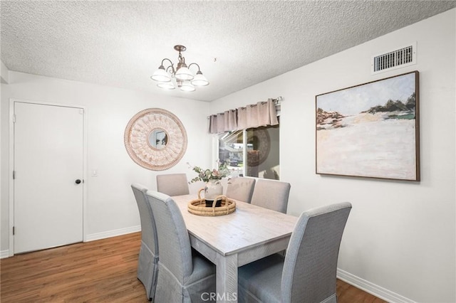 dining room featuring wood finished floors, baseboards, visible vents, a textured ceiling, and a chandelier