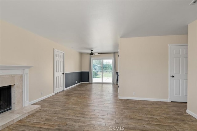 unfurnished living room featuring baseboards, wood finished floors, a ceiling fan, and a premium fireplace