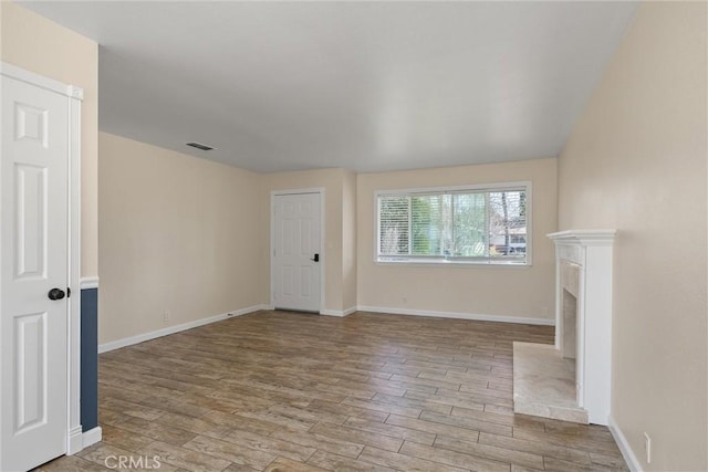 unfurnished living room with a fireplace, wood finished floors, visible vents, and baseboards