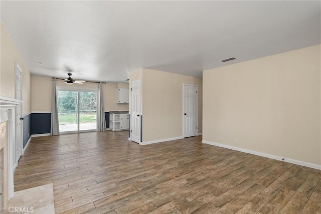 unfurnished living room with visible vents, a ceiling fan, baseboards, and wood finished floors