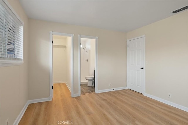 unfurnished bedroom with a walk in closet, visible vents, a closet, light wood finished floors, and baseboards