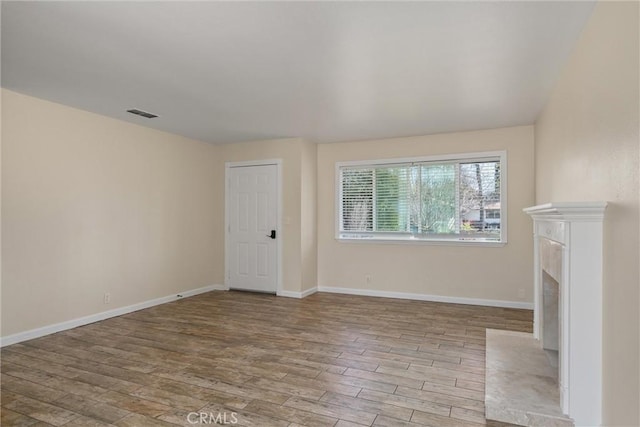 unfurnished living room with visible vents, a fireplace with flush hearth, baseboards, and wood finished floors