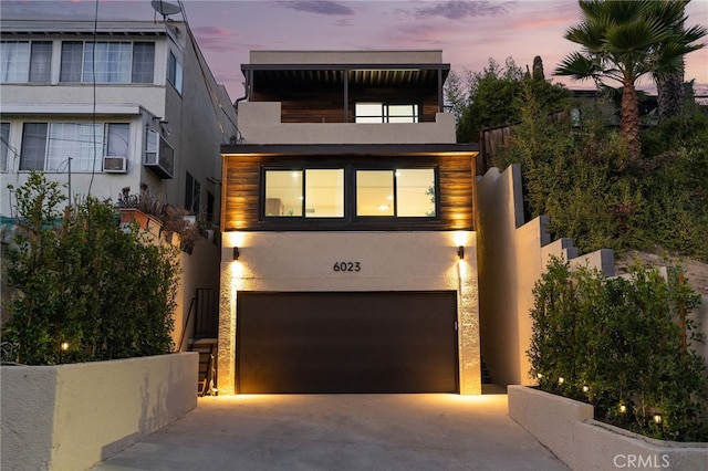 contemporary home with concrete driveway, a balcony, an attached garage, and stucco siding