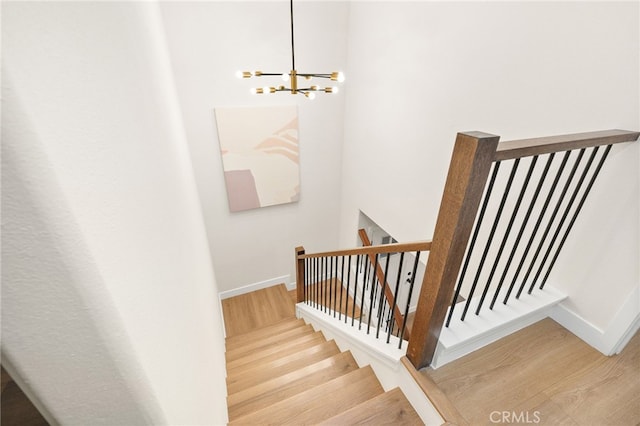 staircase featuring a chandelier, baseboards, and wood finished floors