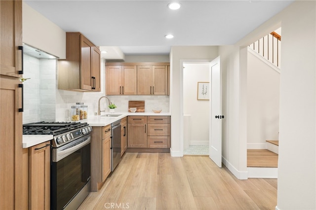 kitchen featuring a sink, decorative backsplash, light countertops, appliances with stainless steel finishes, and light wood-type flooring