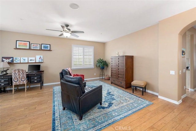 living room with light wood-type flooring, arched walkways, baseboards, and a ceiling fan