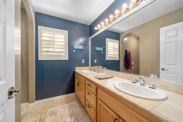 full bath featuring tile patterned flooring, double vanity, baseboards, and a sink