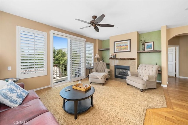 living room with baseboards, a fireplace, arched walkways, and ceiling fan