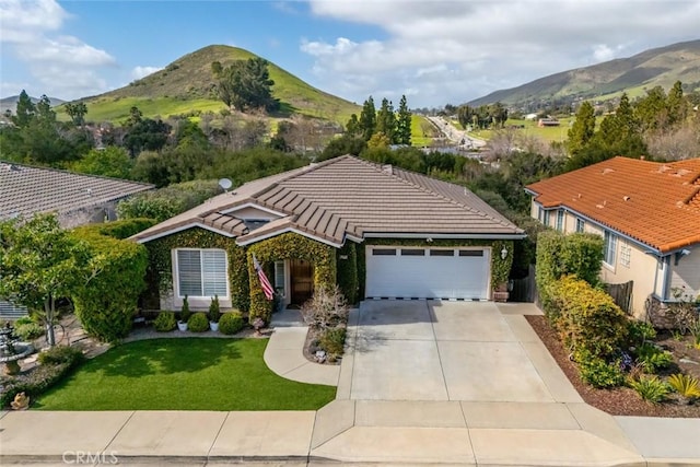 view of front of property featuring a mountain view, a tile roof, driveway, and a garage