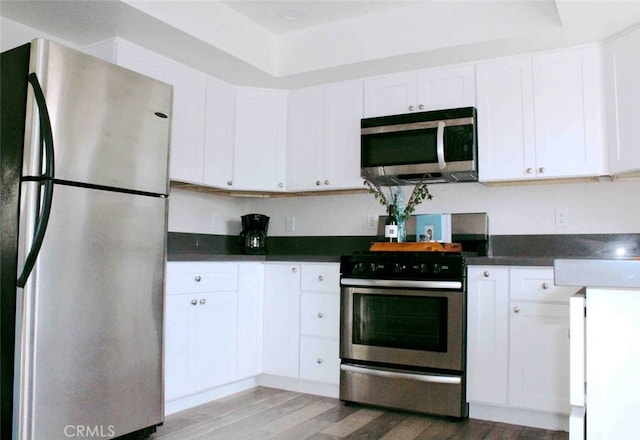 kitchen featuring stainless steel appliances, white cabinetry, dark countertops, and light wood finished floors