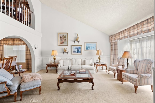 carpeted living area featuring a wainscoted wall, lofted ceiling, arched walkways, a textured ceiling, and a decorative wall