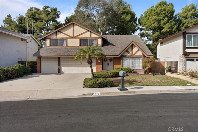 tudor-style house with brick siding, an attached garage, fence, roof with shingles, and driveway