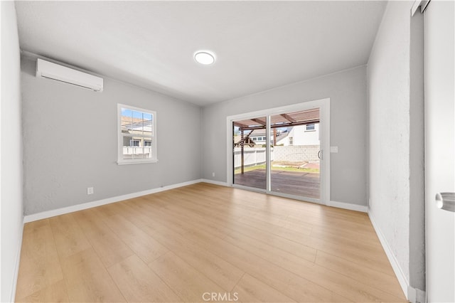 spare room featuring baseboards, light wood-style floors, an AC wall unit, and a healthy amount of sunlight