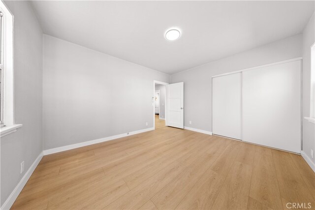 unfurnished bedroom with a closet, baseboards, and light wood finished floors