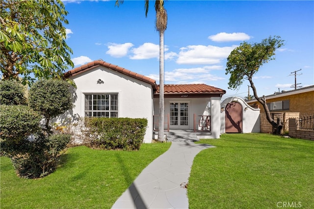 mediterranean / spanish-style home featuring stucco siding, fence, french doors, a front yard, and a tiled roof