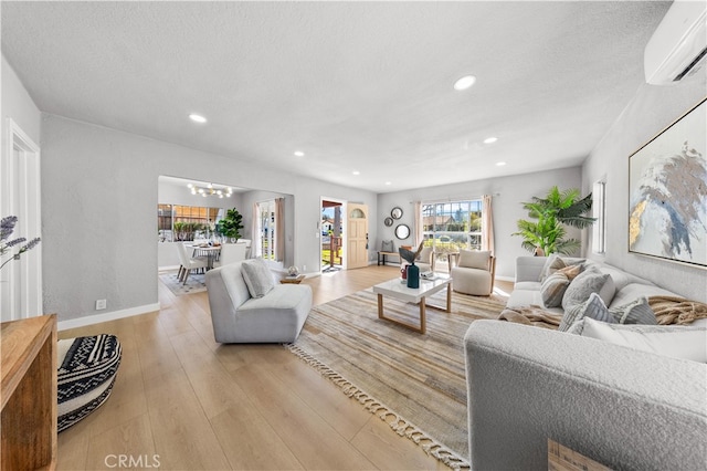 living area featuring a chandelier, light wood-type flooring, recessed lighting, a textured ceiling, and a wall mounted AC