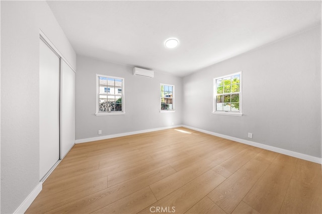 unfurnished bedroom featuring a closet, a wall mounted air conditioner, light wood-type flooring, and baseboards