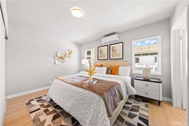 bedroom featuring a wall mounted air conditioner, baseboards, multiple windows, and light wood-style flooring