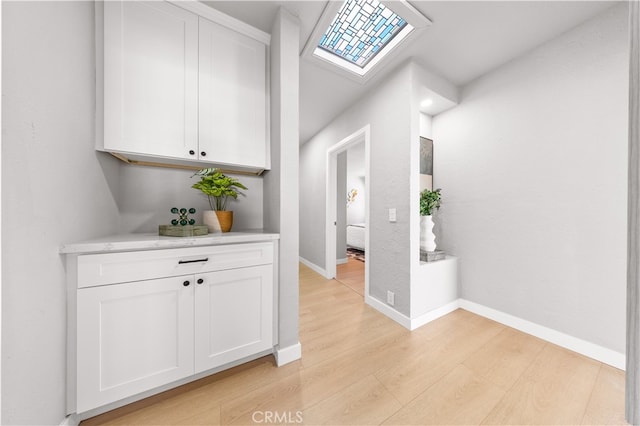 hall featuring light wood finished floors, a skylight, and baseboards