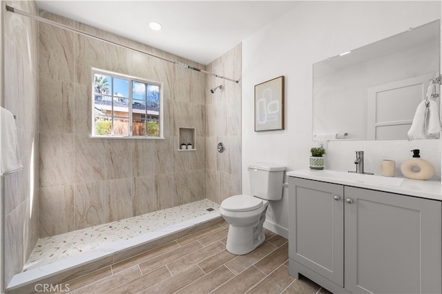 full bathroom with vanity, baseboards, wood finish floors, a tile shower, and toilet