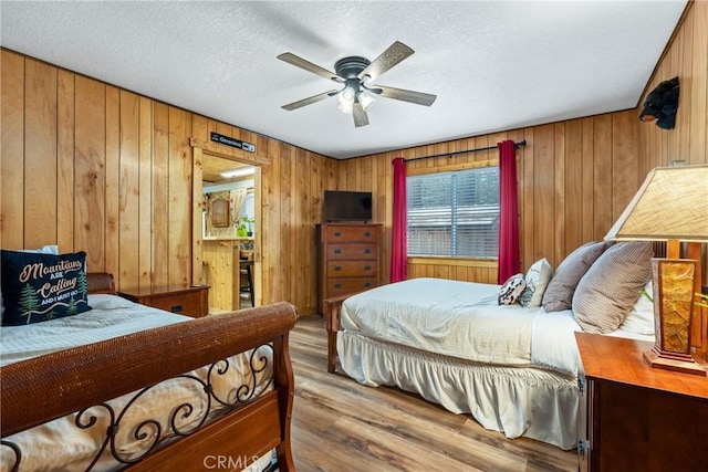 bedroom featuring wood walls, a textured ceiling, a ceiling fan, and wood finished floors