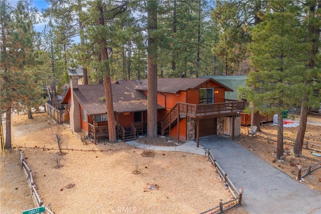 chalet / cabin with driveway, stone siding, stairway, an attached garage, and a wooden deck