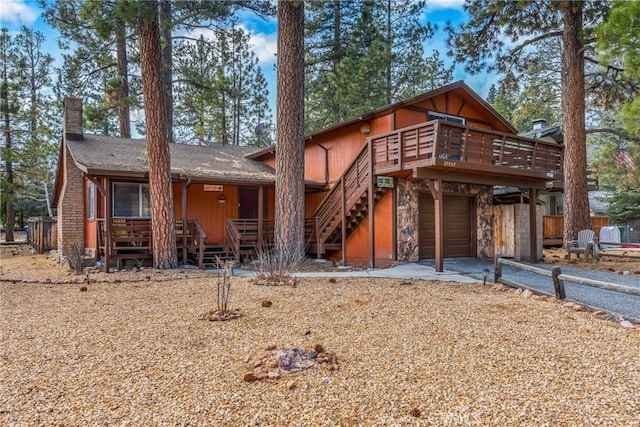 chalet / cabin with driveway, stone siding, a wooden deck, a garage, and a chimney