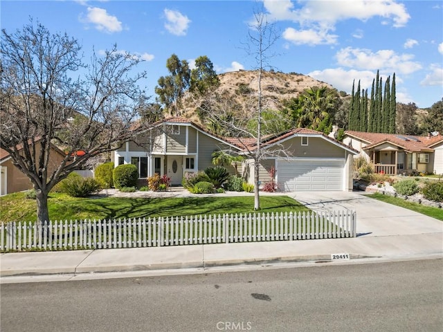 view of front of home with a front lawn, a fenced front yard, concrete driveway, a garage, and a mountain view