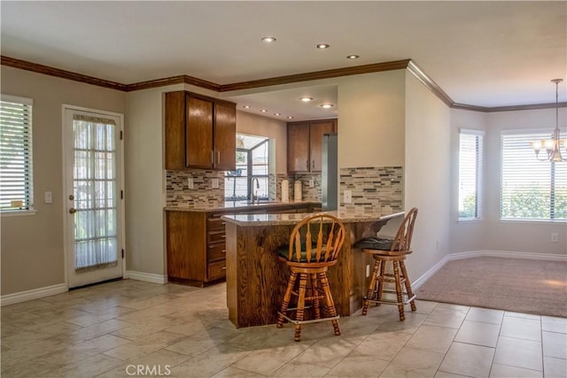 kitchen featuring backsplash, a chandelier, a kitchen bar, brown cabinets, and a sink