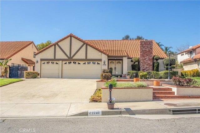 english style home featuring a tiled roof, stucco siding, a garage, driveway, and a gate