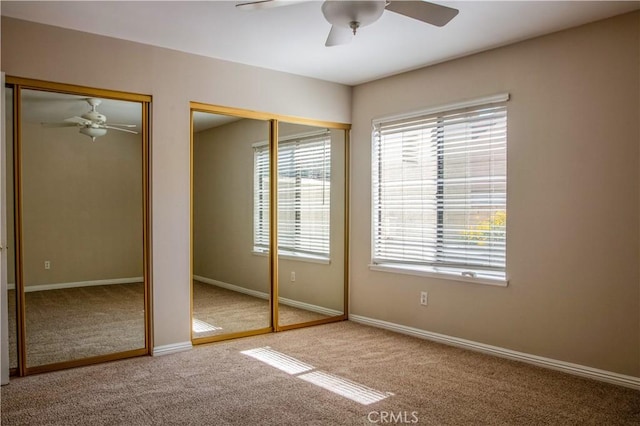 unfurnished bedroom with baseboards, multiple closets, carpet floors, and ceiling fan