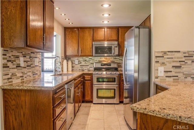 kitchen with a sink, brown cabinetry, light stone countertops, and stainless steel appliances