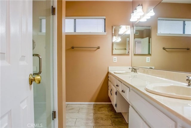 bathroom with double vanity, a shower stall, baseboards, and a sink