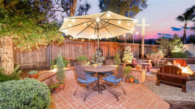 patio terrace at dusk with outdoor dining area, a fire pit, and a fenced backyard